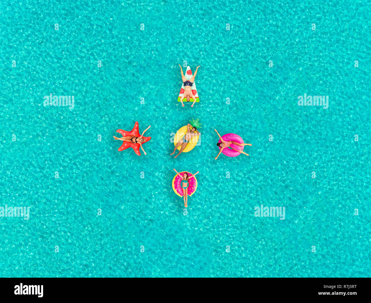 Aerial view of people floating on inflatable pizza, flamingo, star, pineapple and donut shaped mattresses, in formation. Stock Photo