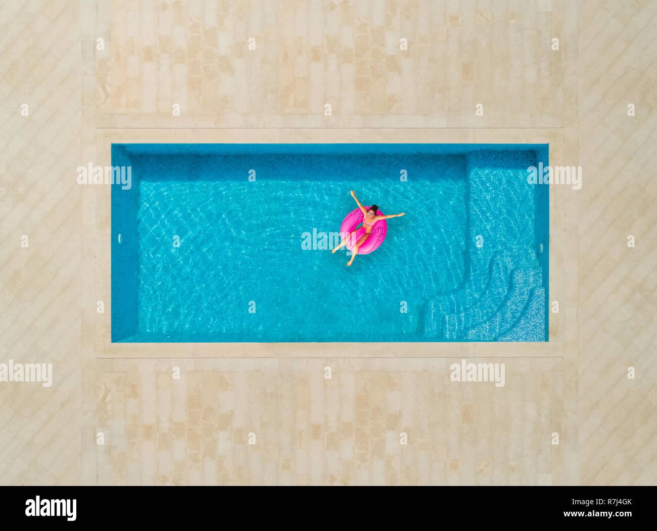 Aerial view of woman on a inflatable flamingo mattress in swimming pool. Stock Photo