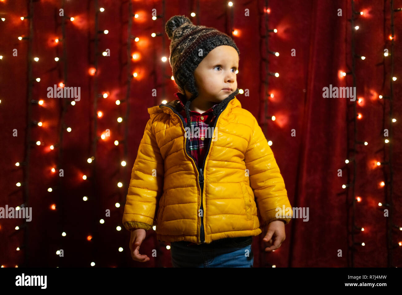 Young boy posing serious in front of lights wall at Christmas market. Stock Photo