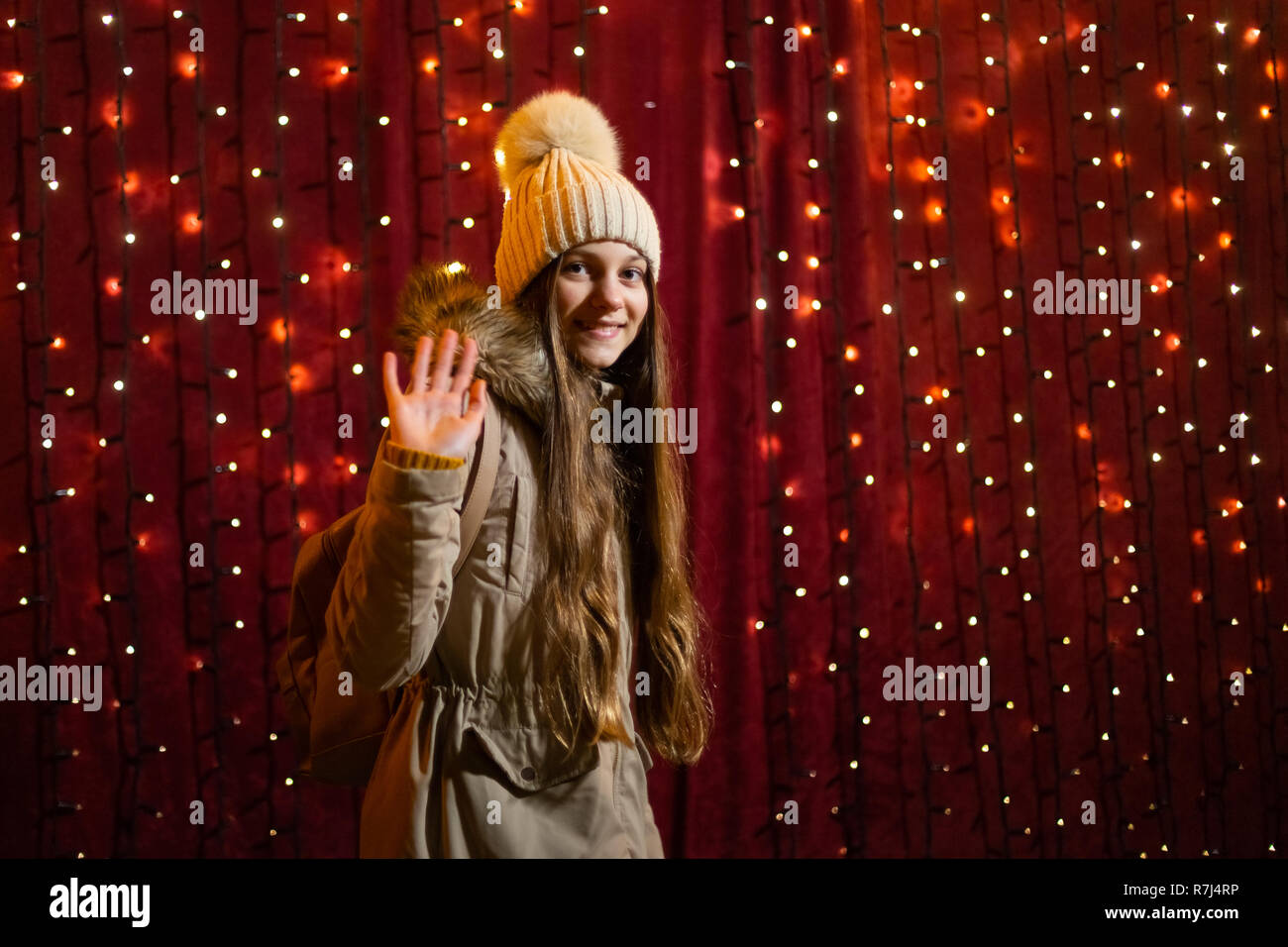 Cute teenager posing and waving in front of lights wall at Christmas market. Stock Photo