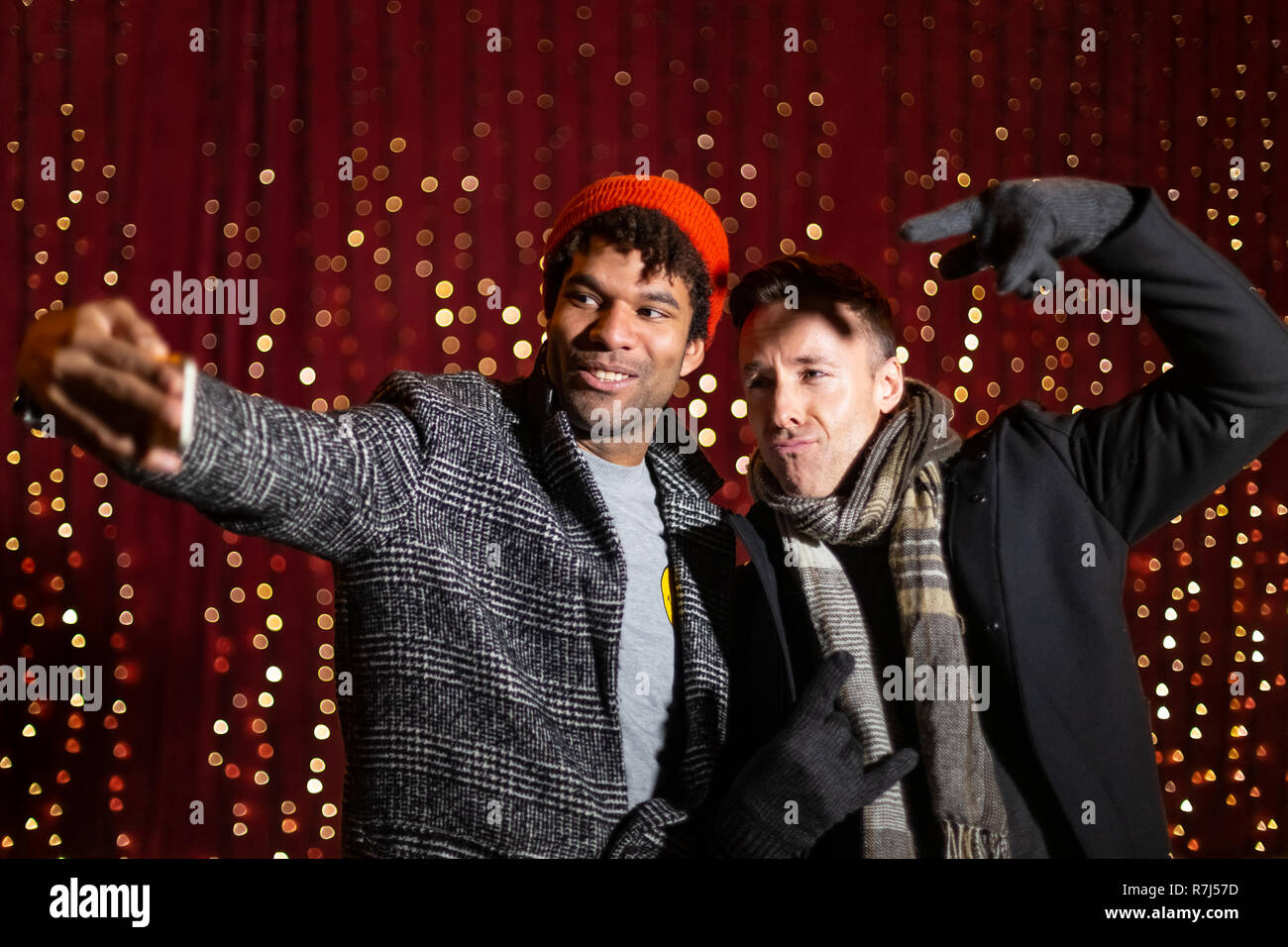 Two friends taking selfie in front of light wall at Christmas market. Stock Photo