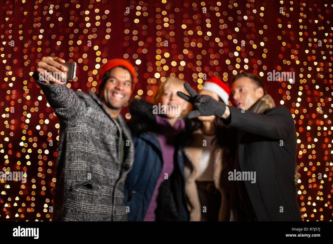 Group of friends out of focus taking selfie in front of light wall at Christmas market. Stock Photo