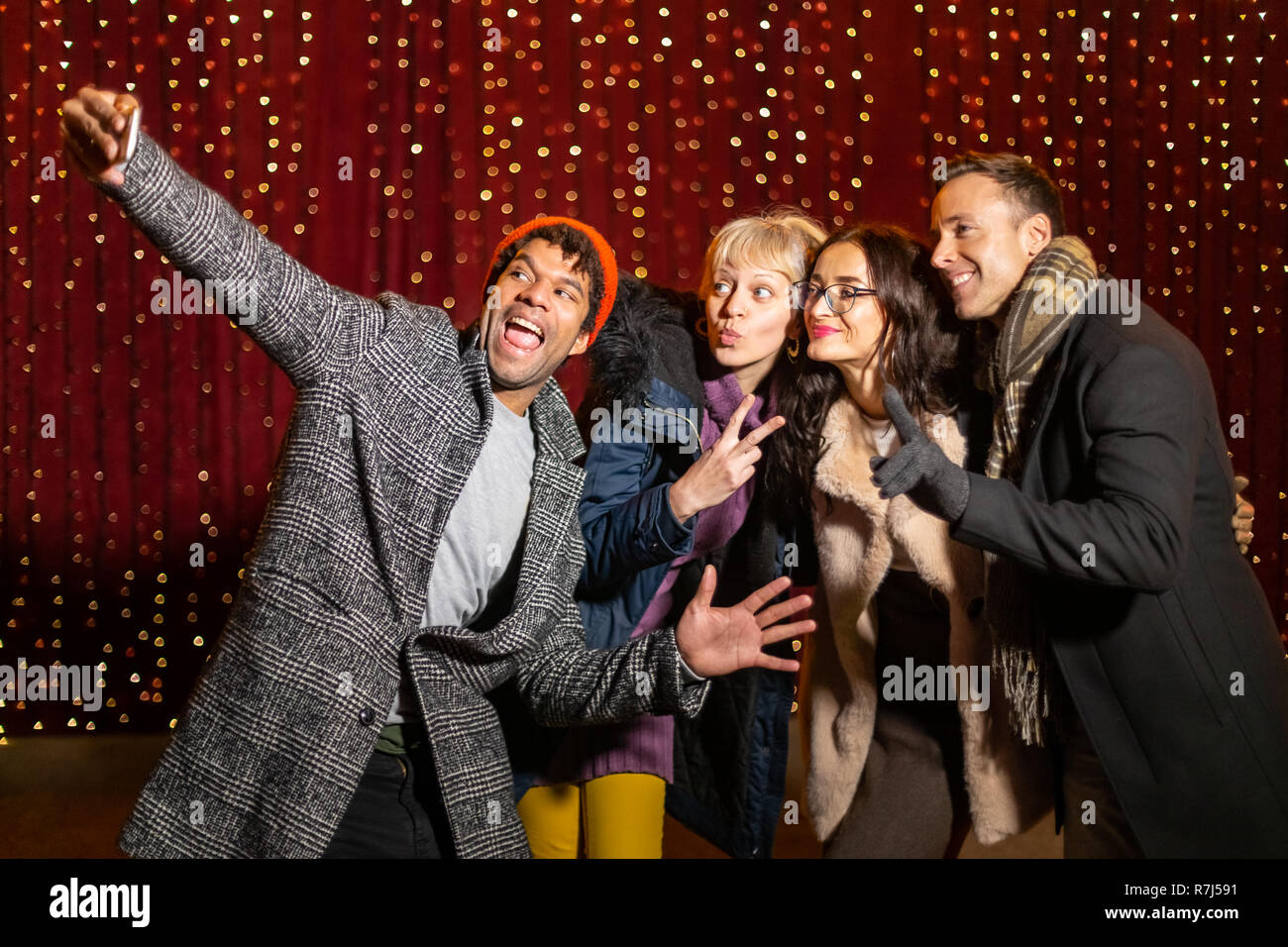 Group of friends taking funny selfie in front of light wall at Christmas market. Stock Photo