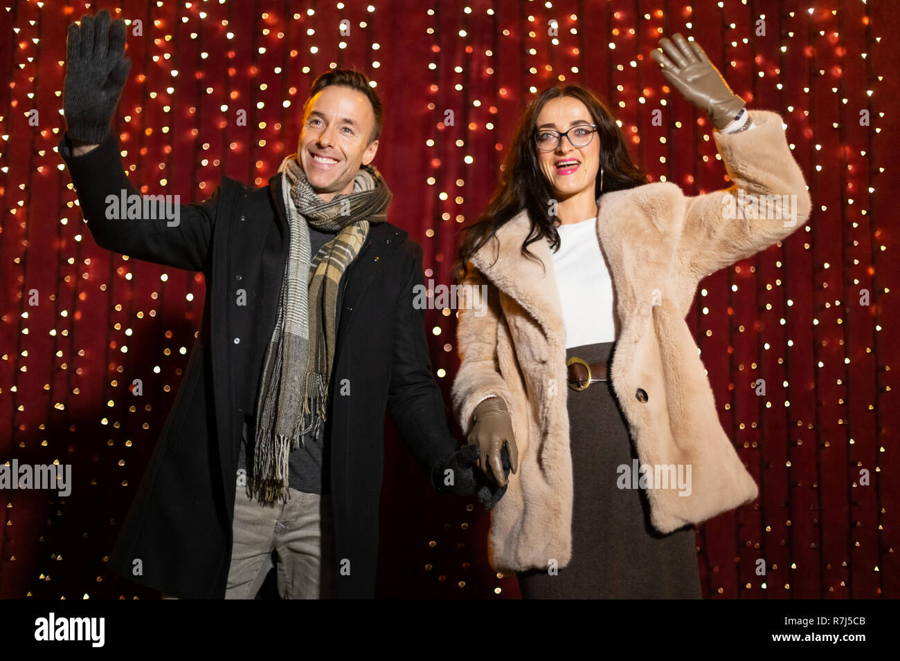 Couple waving for photo in front of light wall at Christmas market. Stock Photo