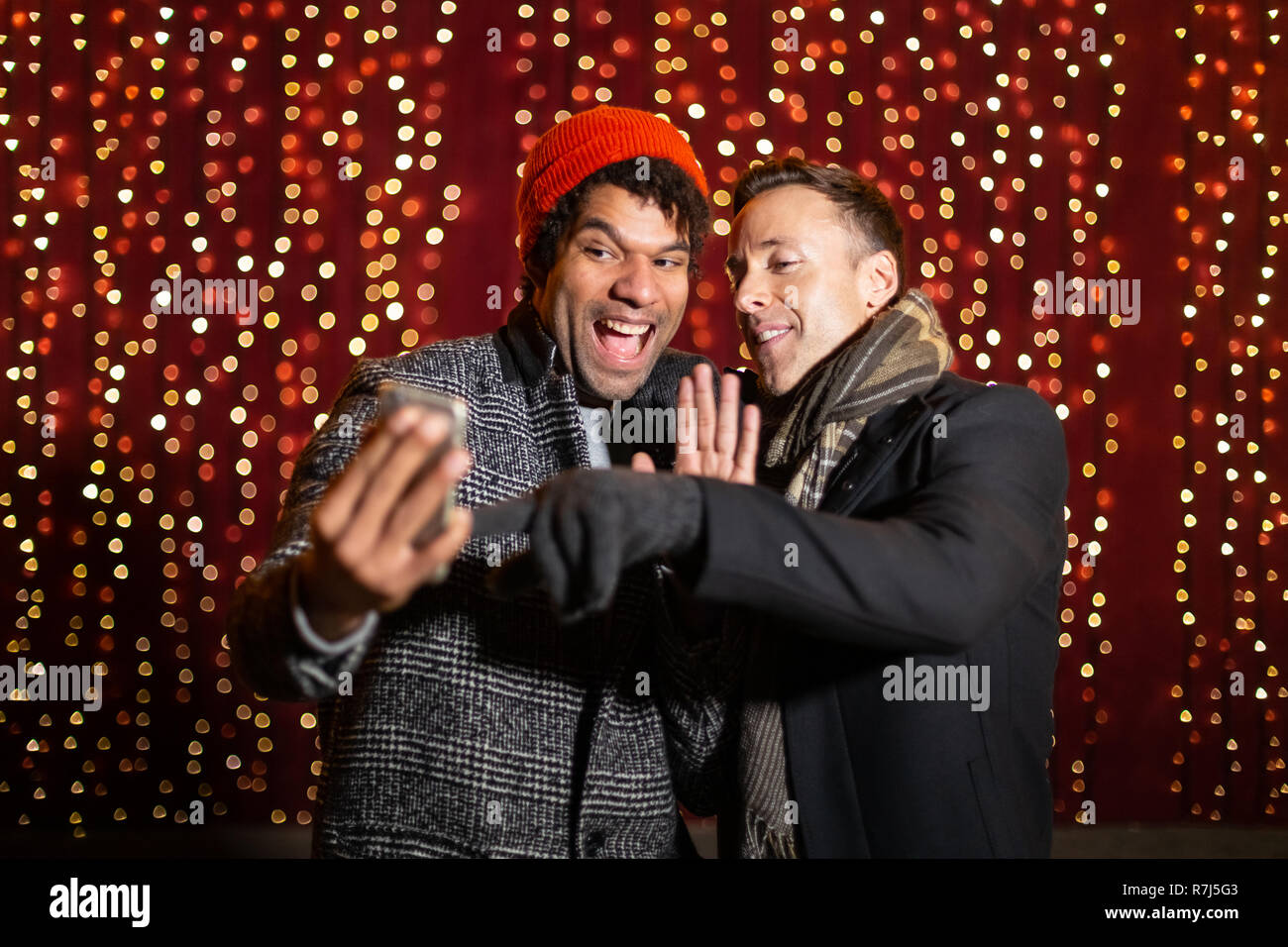 Two friends doing a video chat in front of light wall at Christmas market. Stock Photo