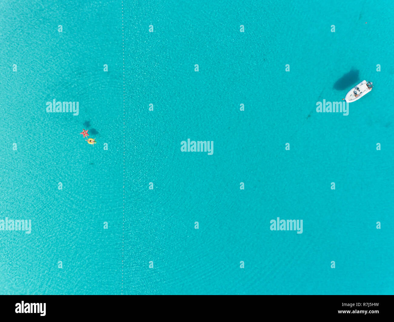 Aerial view of two people floating in open sea on inflatables by white dingy. Stock Photo