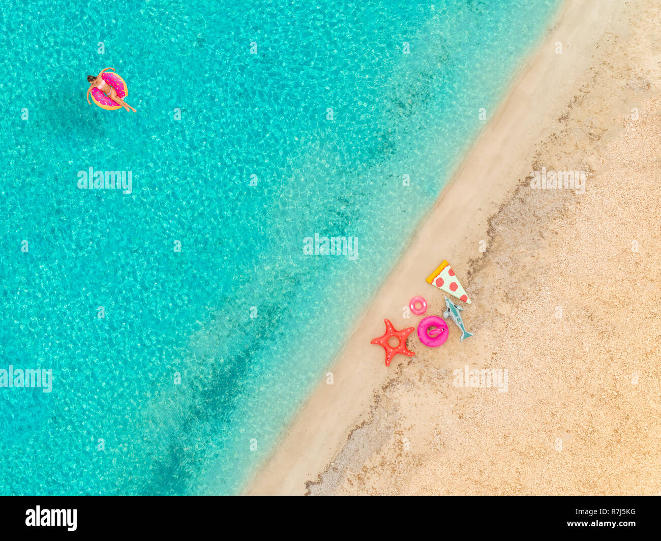 Aerial view of woman floating on inflatable donut mattress by sandy beach and inflatable rings. Stock Photo