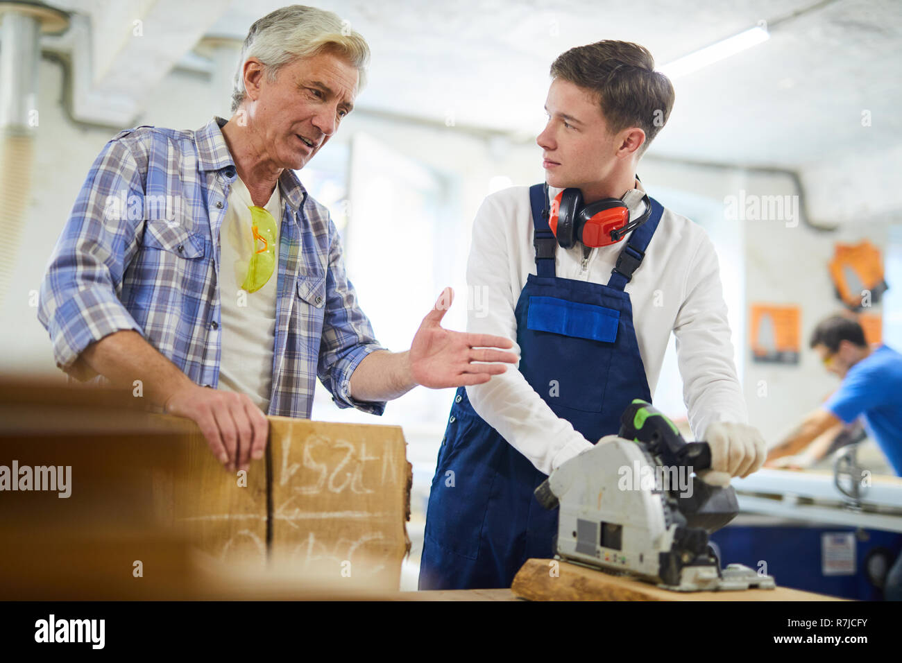 Serious carpenter giving advice to intern in workshop Stock Photo
