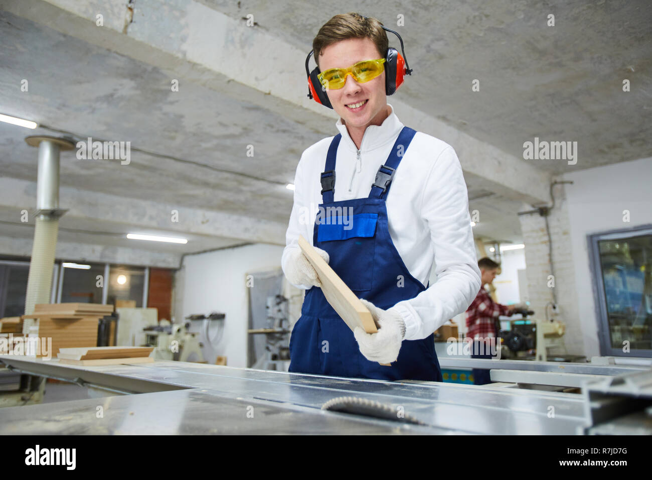 Cheerful young carpenter with wooden board in workshop Stock Photo