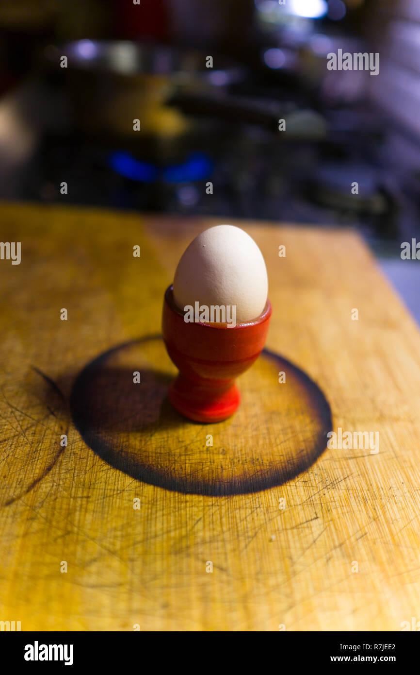 boiled egg in red ceramic egg cup sitting within burnt circle on bamboo