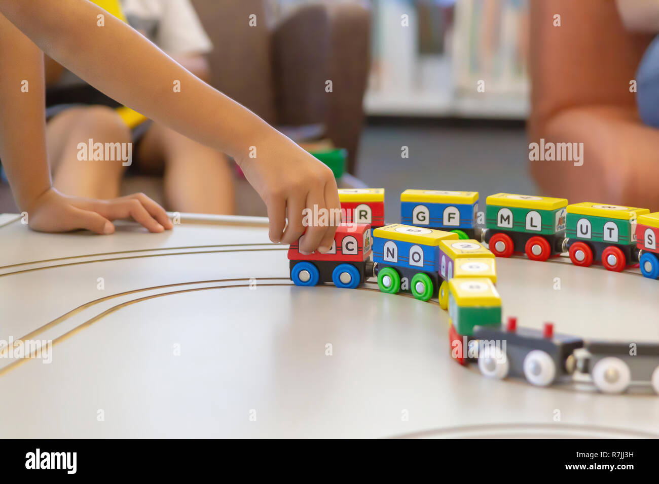 A child's hand pulls the train along. The colorful train with letters of the alphabet and numbers painted all around are magnetically connected. Stock Photo