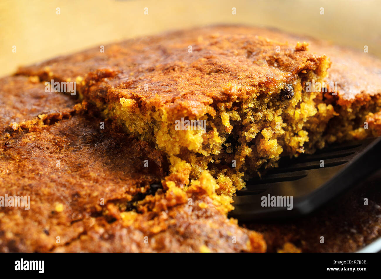 A crumbly square slice of freshly baked carrot cake being lifted from baking dish for serving. Close up just above eye level. Stock Photo