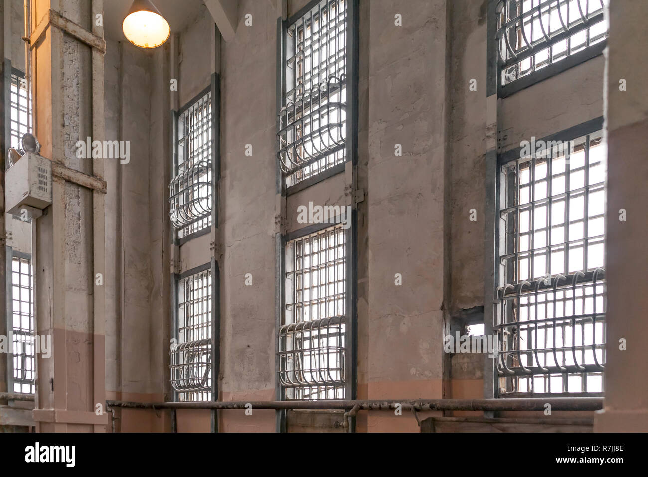 Old correctional penitentiary jailhouse multilevel wall of windows covered with solid steel vertical and horizontal bars painted in neutral tones. Stock Photo