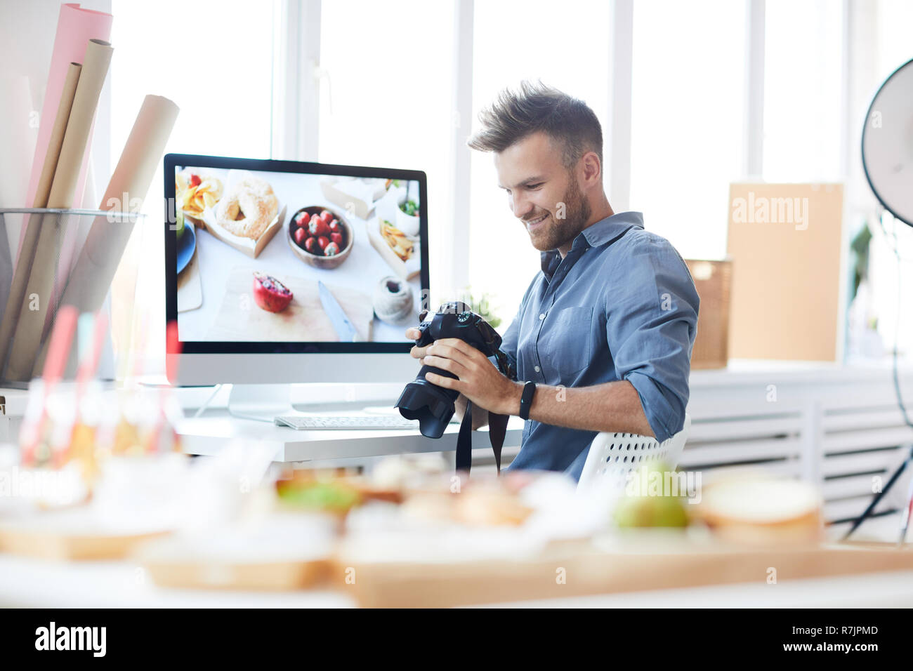 Portrait of smiling photographer holding camera and looking at pictures on set in studio, copy space Stock Photo