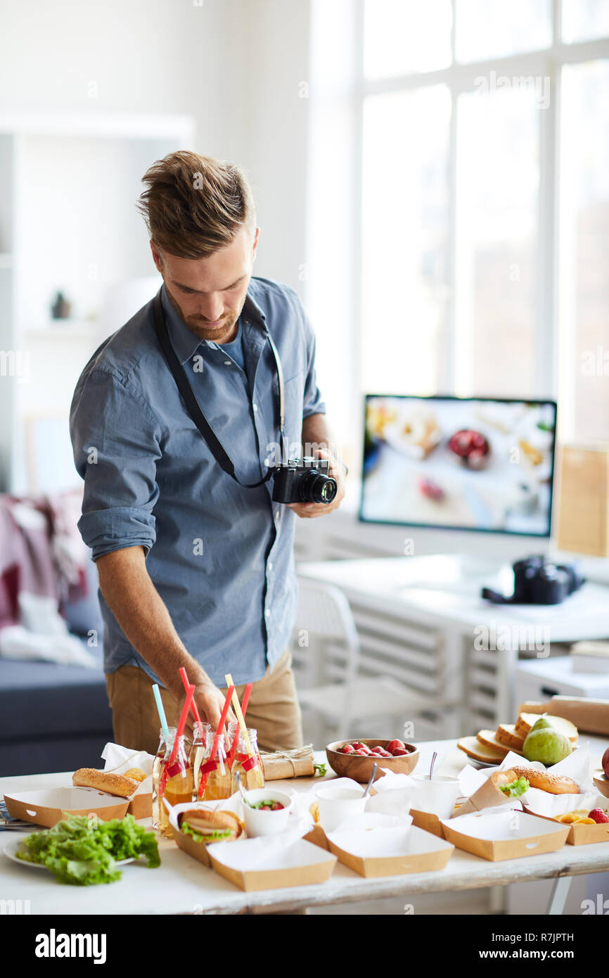 Waist up portrait of smiling photographer taking pictures of party table with food Stock Photo