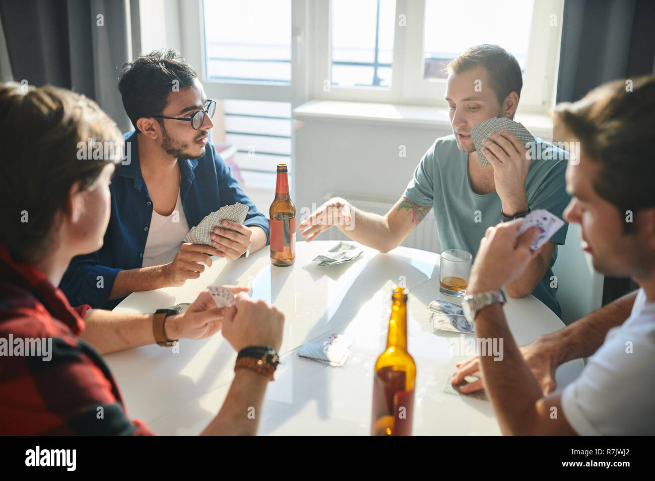 Group of male friends playing cards at the table and drinking alcohol at home Stock Photo