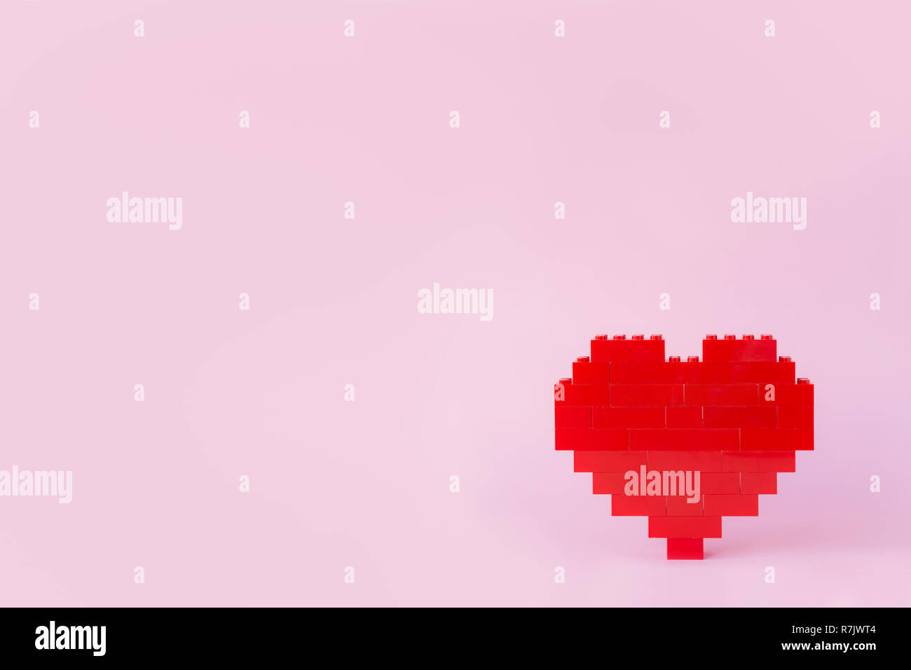 Red heart made of toy building bricks, viewed from the front, on pink background. Copy space. Stock Photo