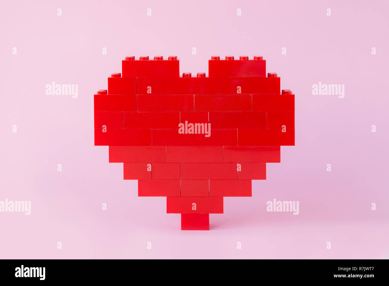 Red heart made of toy building bricks, viewed from the front, on pink background. Stock Photo
