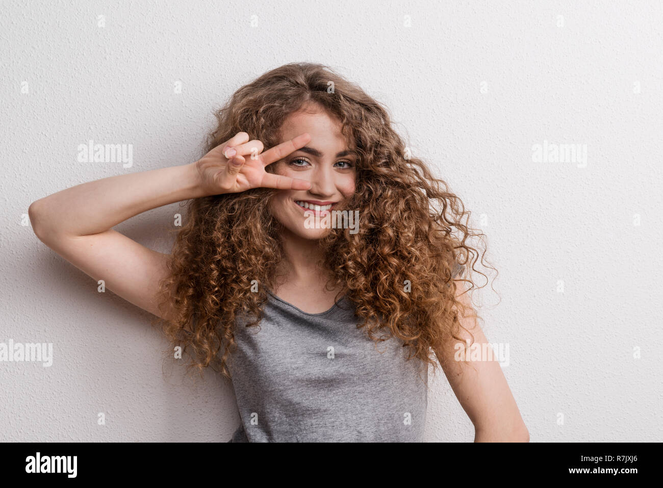 Young beautiful cheerful woman in studio, fingers forming V. Stock Photo
