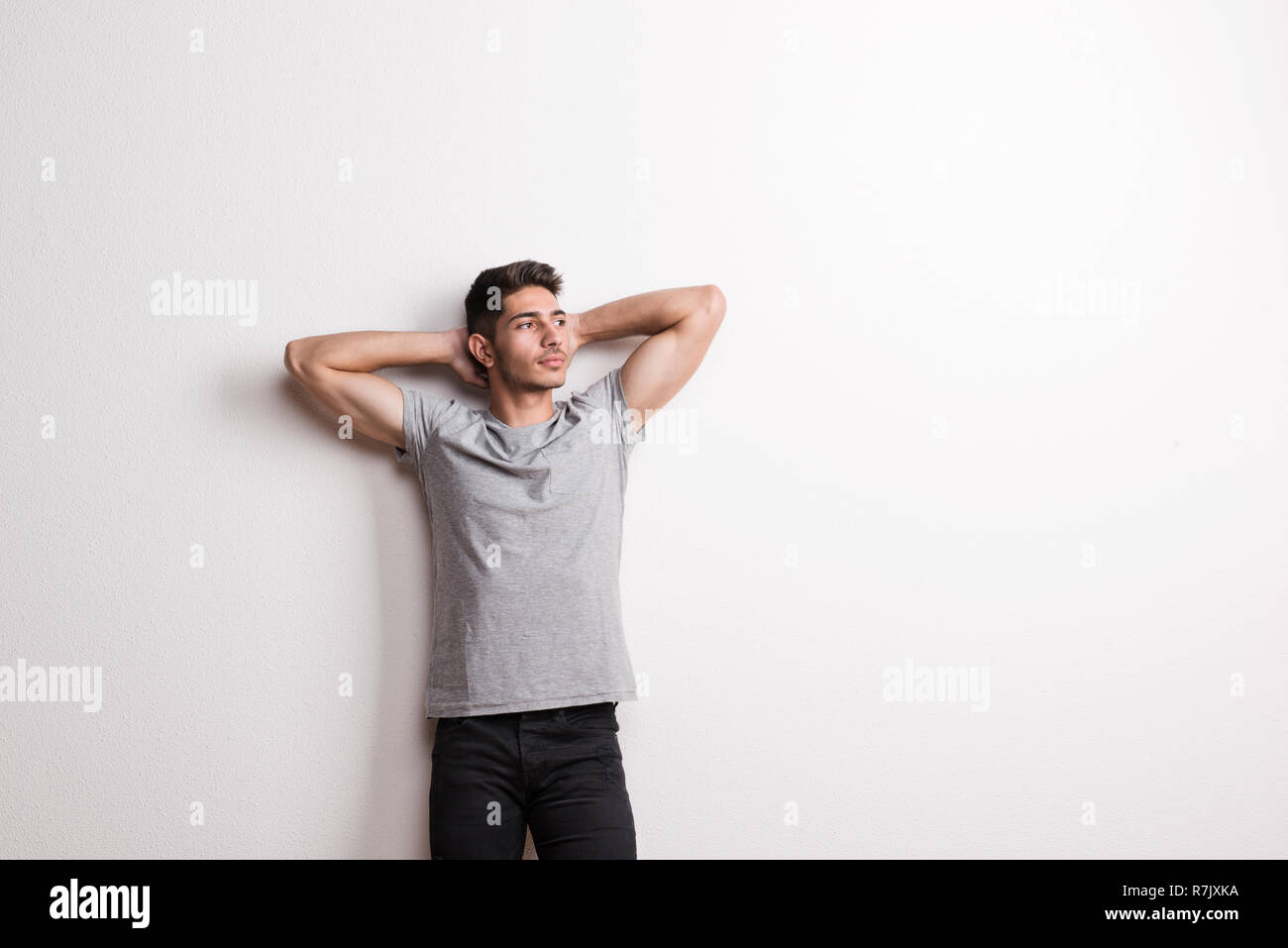 Cheerful young hispanic man standing in a studio, hands behind head. Copy space. Stock Photo