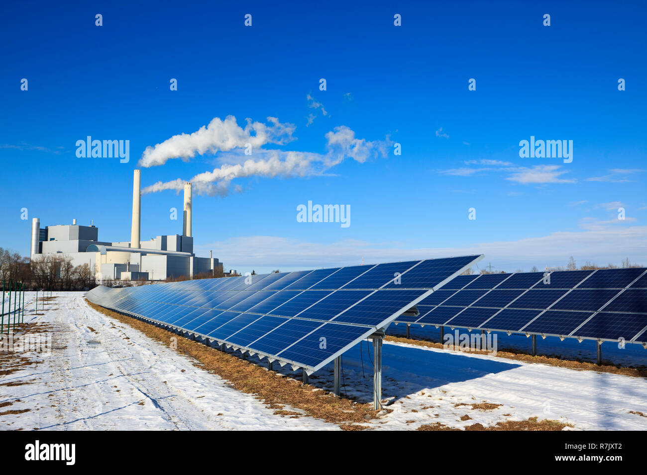 Alternative energy - rack of brand new solar panels. Thermal power plant in  the background. Blue sky reflecting on the panels Stock Photo - Alamy