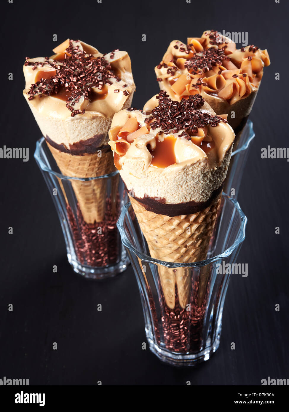 Three caramel ice cream cones, set in glasses filled with sugar