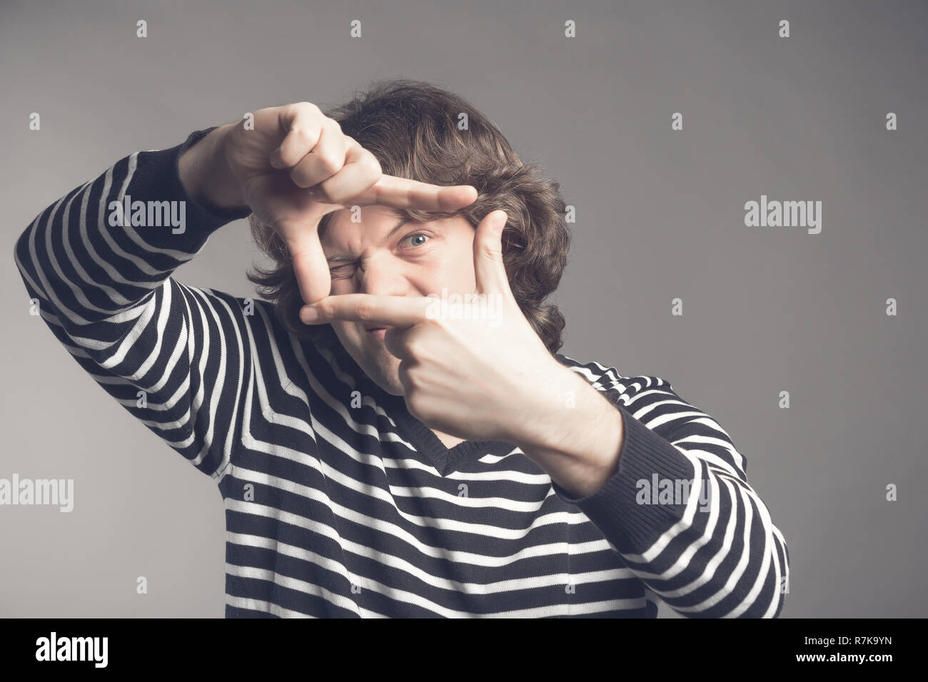 Young handsome man focusing with fingers, framing with hands isolated on grey background. Close up portrait. Stock Photo