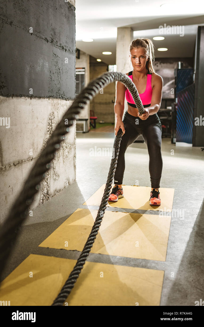 Young woman doing strength training using heavy ropes at the gym