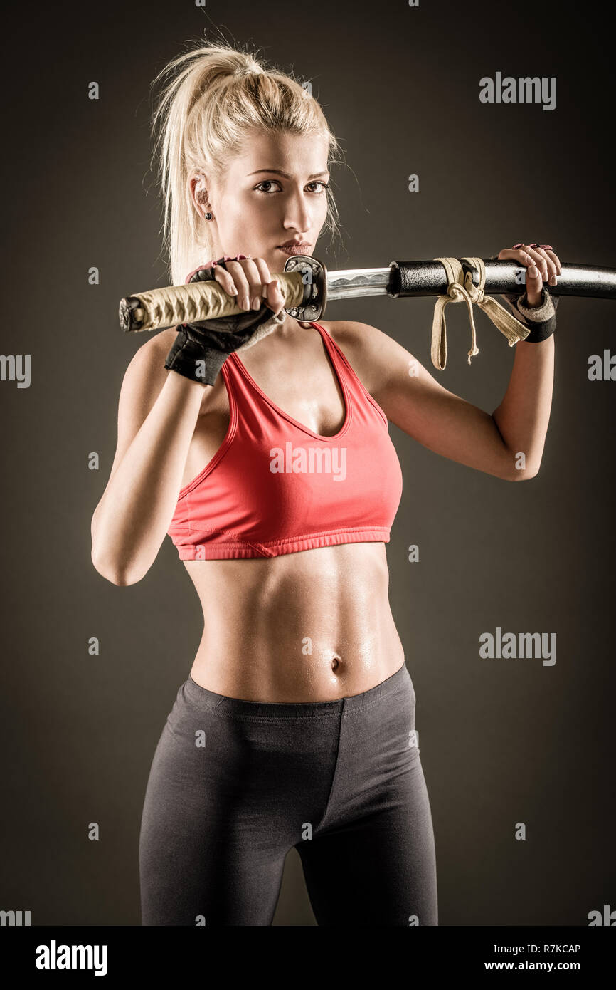 Pretty girl with a serious expression on her face drawing katana and looking at the camera. Stock Photo