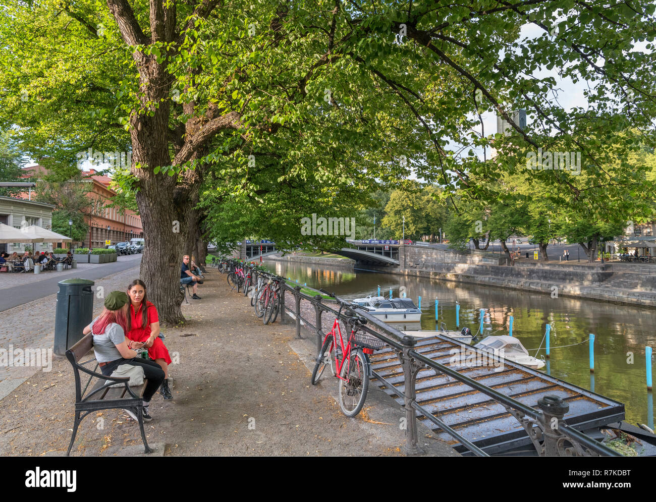 Two young women sitting on the banks of the River Aura (Aurajoki) in the historic centre, Turku, Finland Stock Photo