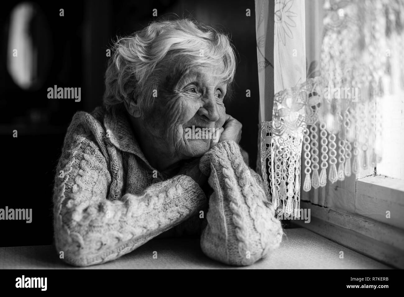 An elderly woman sits and looks out the window. Stock Photo
