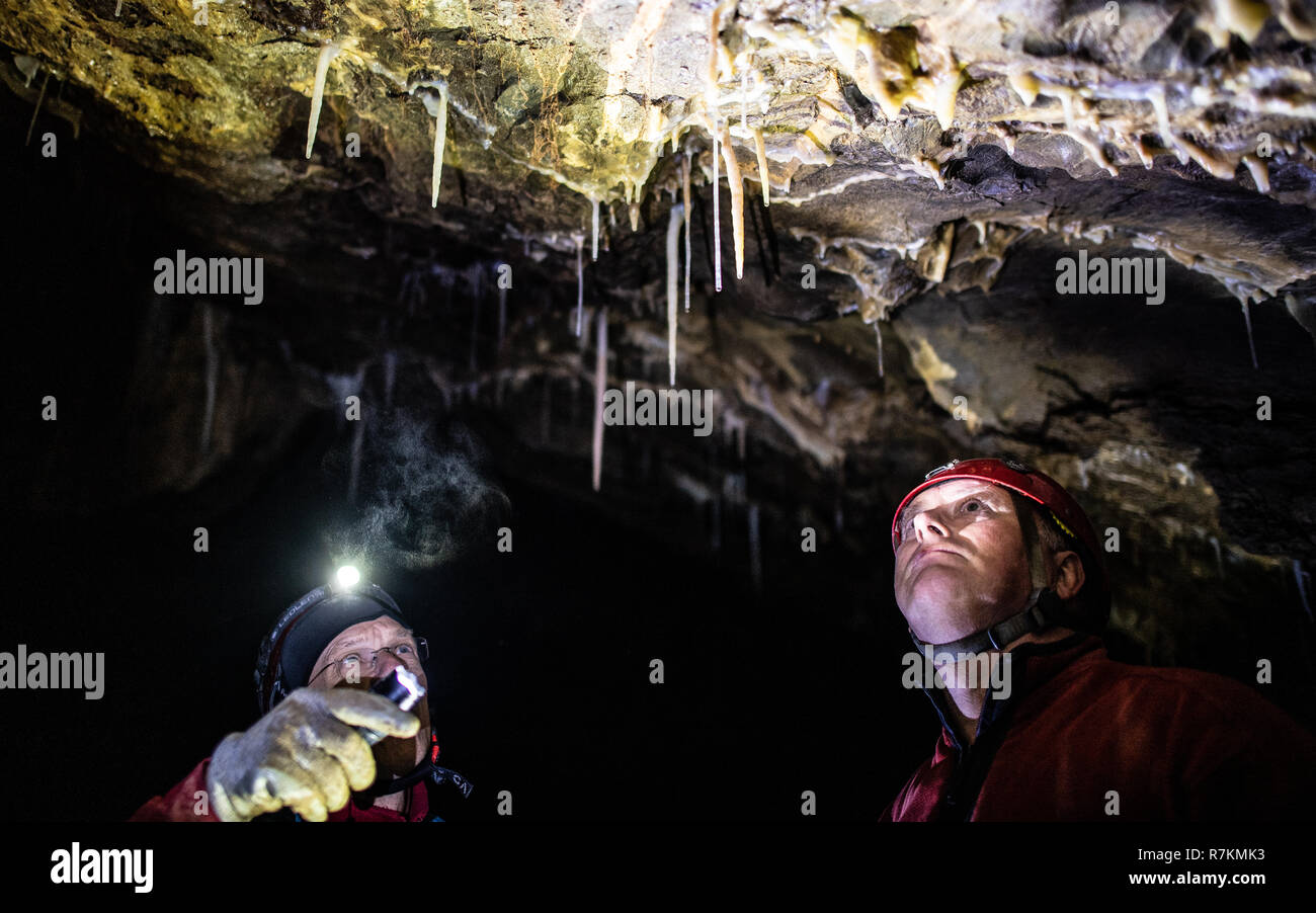 10 December 2018, North Rhine-Westphalia, Bad Wünnenberg: Cave explorers Andreas Schudelski (r) and Stefan Henscheid use their torches to illuminate the greenish-blue stalactites hanging from the ceiling of the Malachite Cathedral stalactite cave. The stalactite cave in the middle of a producing quarry has been saved for the time being. As a spokeswoman of the Paderborn district reported on 10.12.2018, an application by the quarry operator to dismantle the cave, which is under nature conservation, was rejected. Due to its enormous dimensions and the blue and green stalactites, the cave occupie Stock Photo