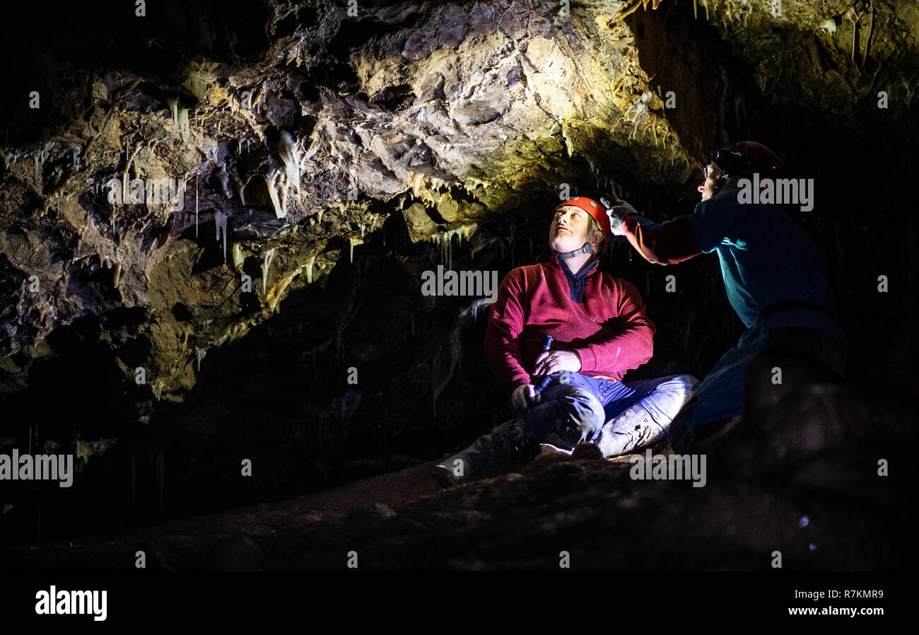 10 December 2018, North Rhine-Westphalia, Bad Wünnenberg: Cave explorers Andreas Schudelski (l) and Stefan Henscheid use their torches to illuminate the greenish-blue stalactites hanging from the ceiling of the Malachite Cathedral stalactite cave. The stalactite cave in the middle of a producing quarry has been saved for the time being. As a spokeswoman of the Paderborn district reported on 10.12.2018, an application by the quarry operator to dismantle the cave, which is under nature conservation, was rejected. Due to its enormous dimensions and the blue and green stalactites, the cave occupie Stock Photo