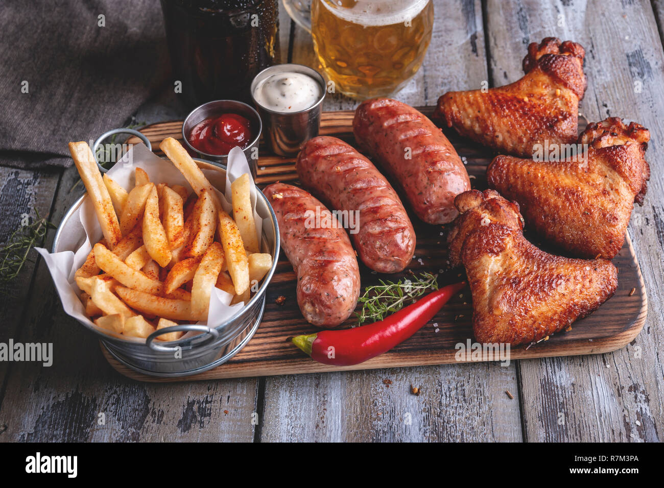 Grilled chicken wings,sausages french fries, white and red sauce on a wooden surface. Stock Photo
