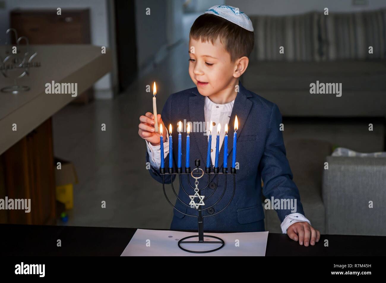 Cute Caucasian Jewish boy lighting candles on a traditional Hanukkah