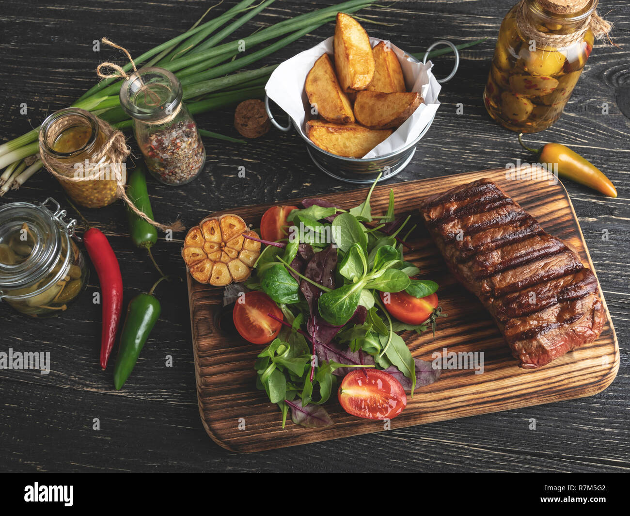 Grilled steak on the board served with herbs, fried potatoes, spices on a black surface Stock Photo