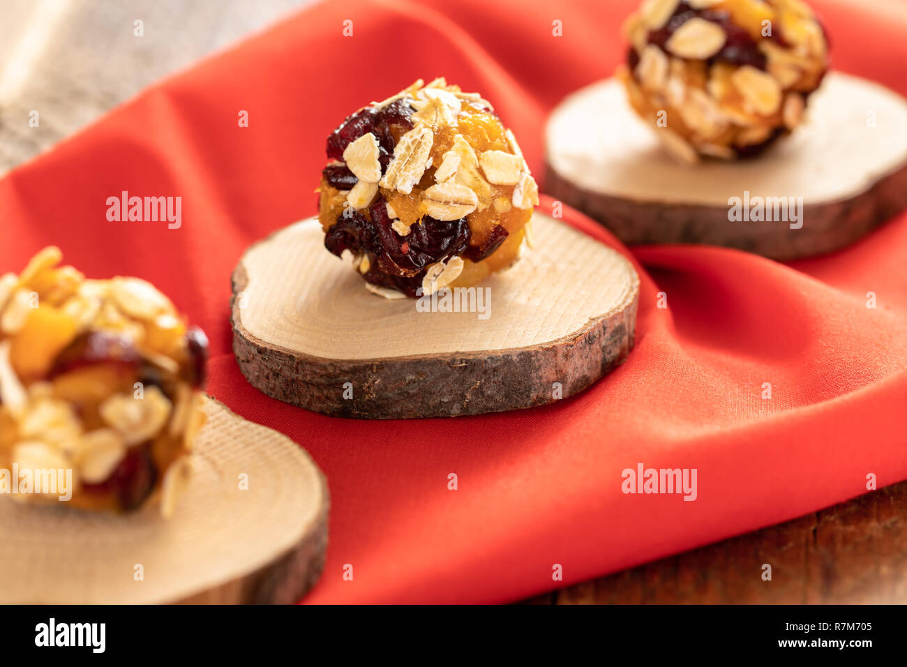 Three homemade energy ball are lying diagonally in row on wooden saw cut on red fabric. Stock Photo