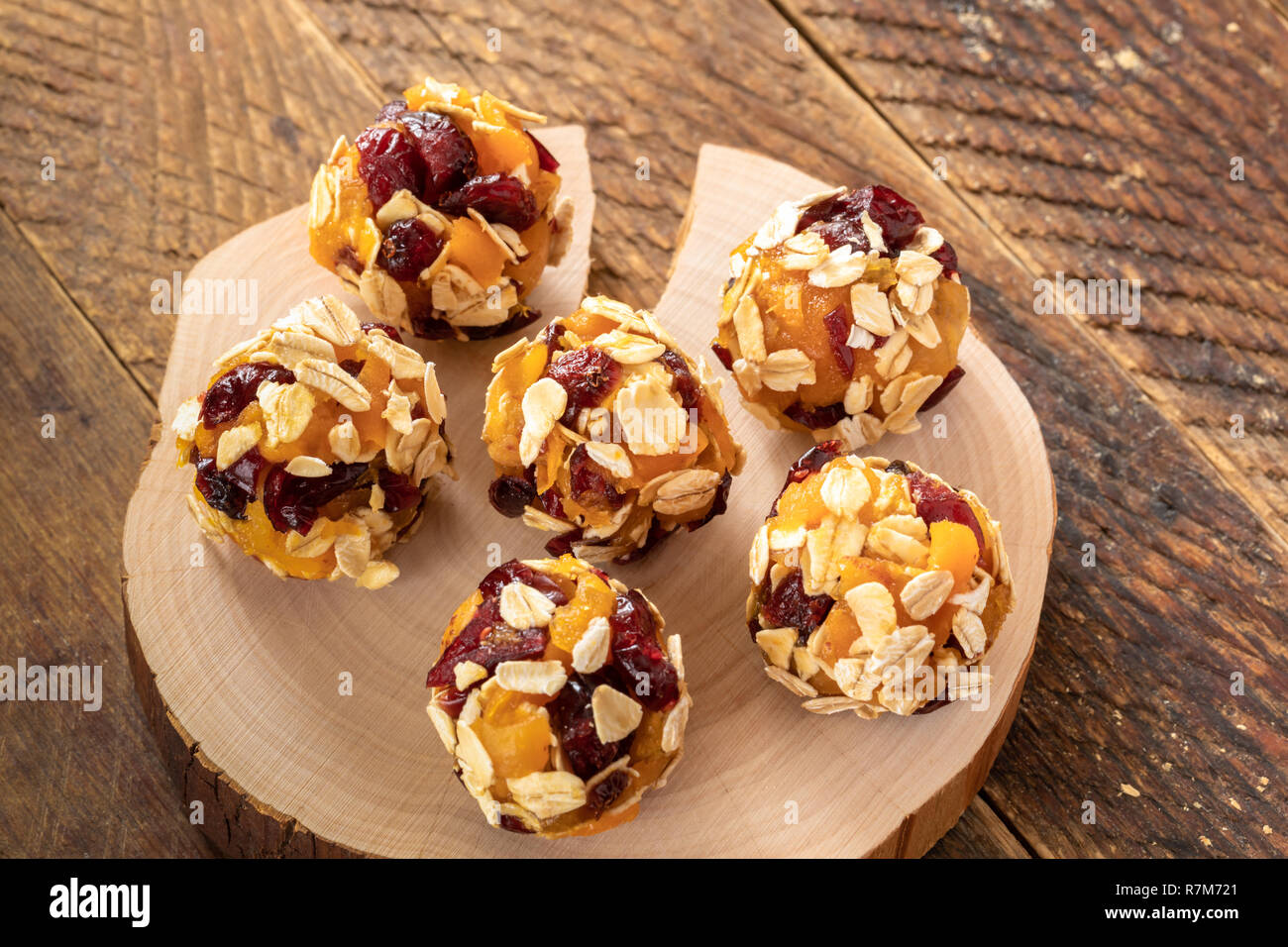 Six homemade energy balls are lying on wooden saw cut on brown wooden table. Stock Photo