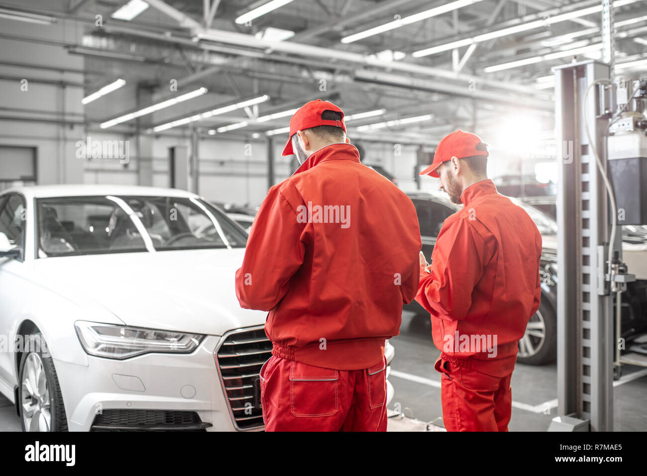 Two auto mechanics in red uniform standing together in front of the luxury car at the car service Stock Photo