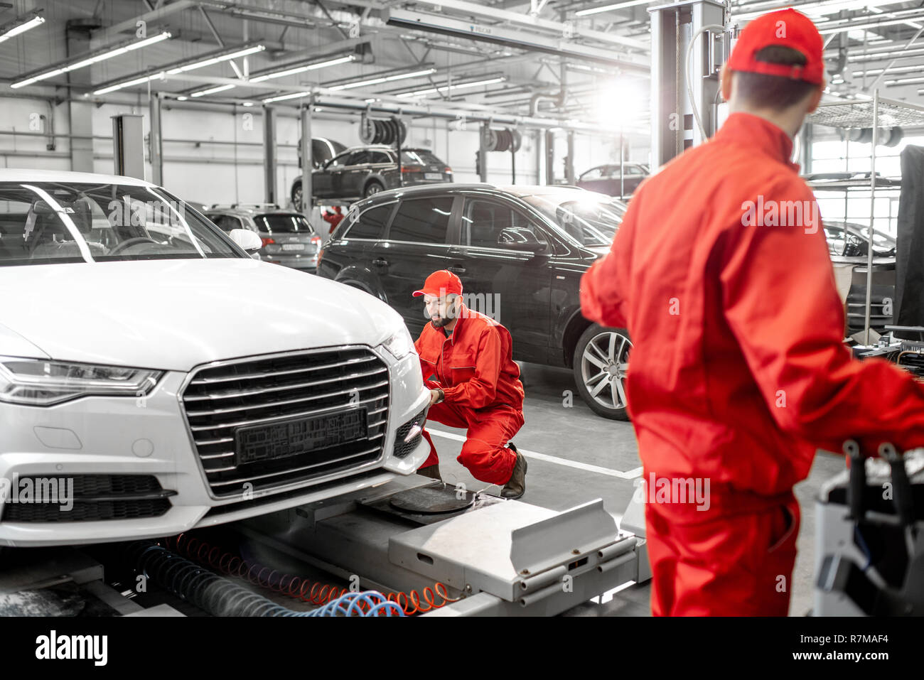 Two handsome auto mechanics in red uniform making wheel alignment with professional tools and computer at the car service Stock Photo