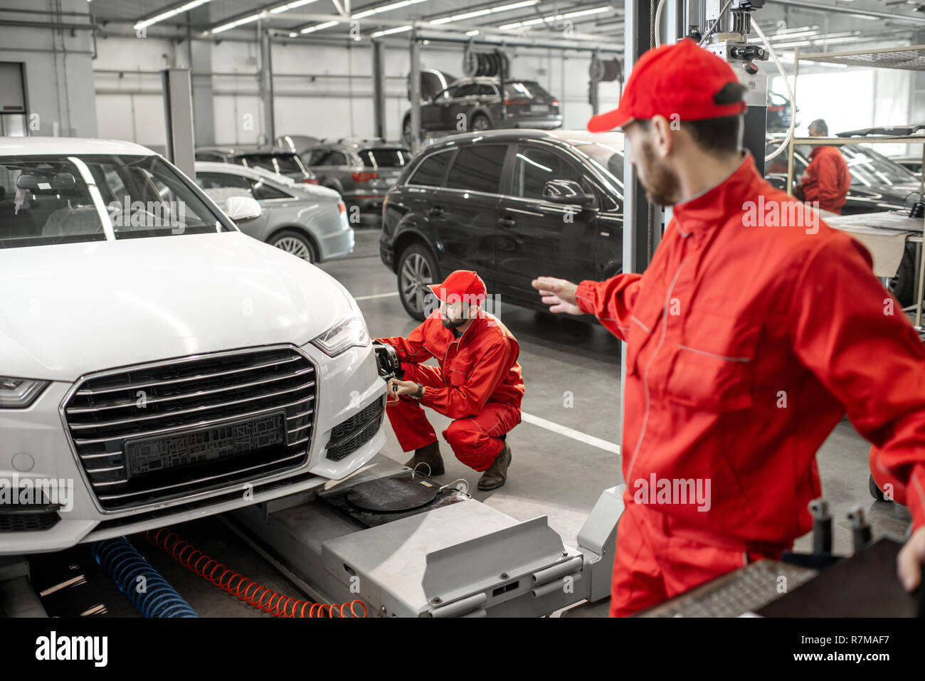 Two handsome auto mechanics in red uniform making wheel alignment with professional tools and computer at the car service Stock Photo