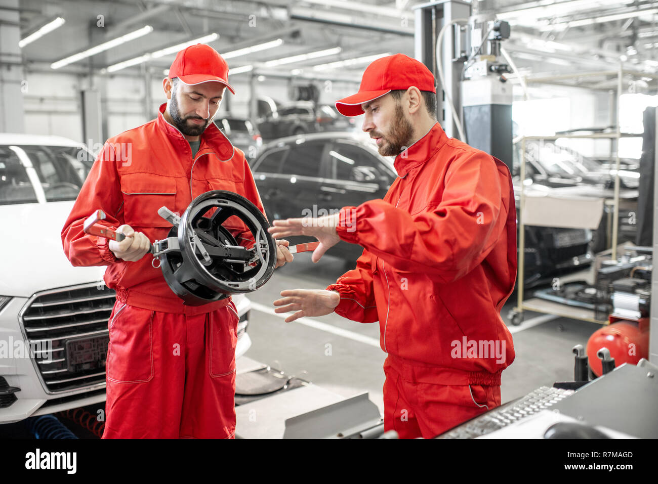 Two handsome auto mechanics in red uniform making wheel alignment with professional tools and computer at the car service Stock Photo