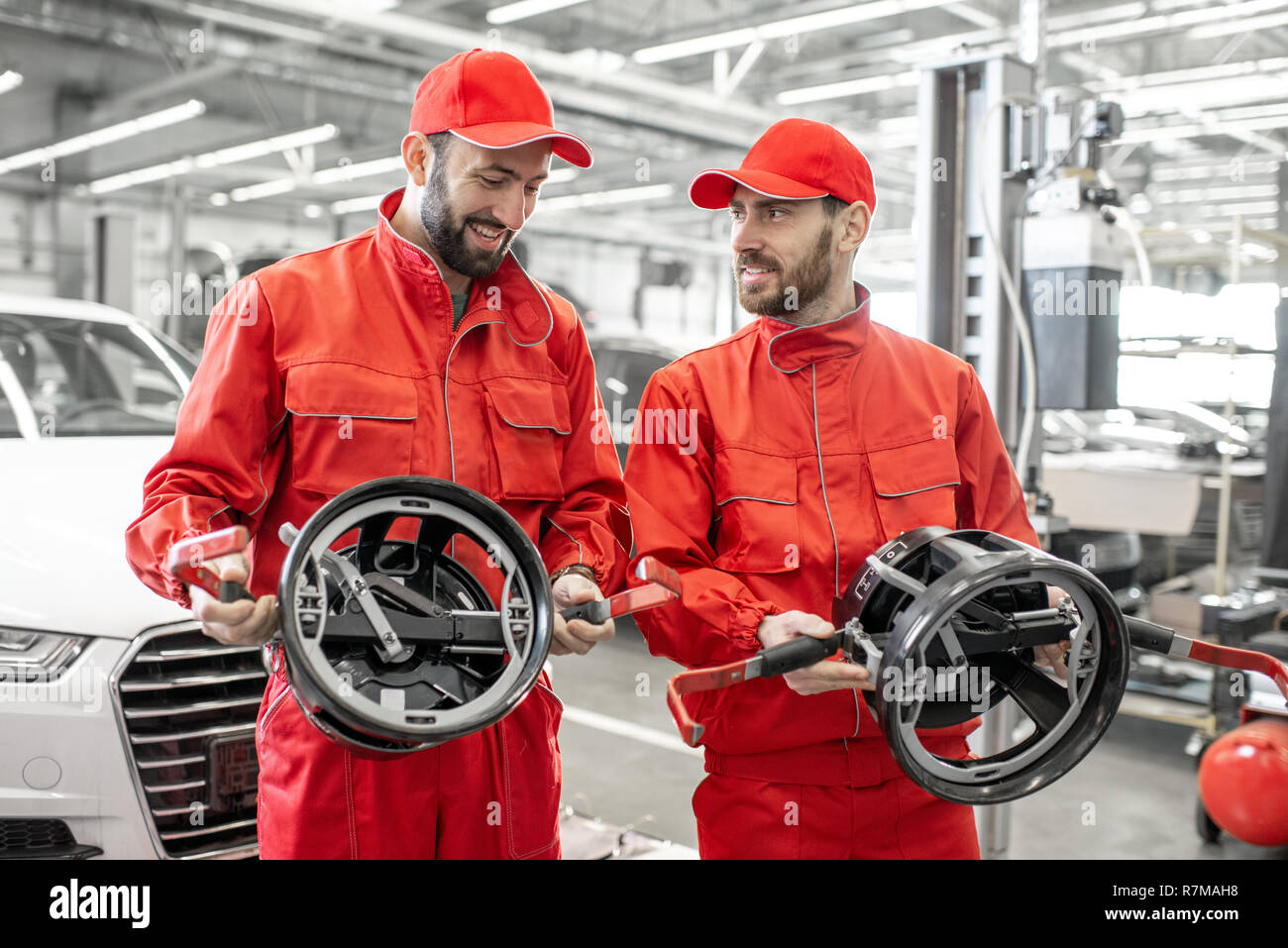 Portrait of a two auto mechanics in red uniform standing with disks for wheel alignment at the car service Stock Photo