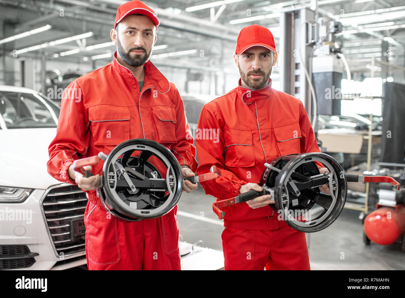 Portrait of a two auto mechanics in red uniform standing with disks for wheel alignment at the car service Stock Photo