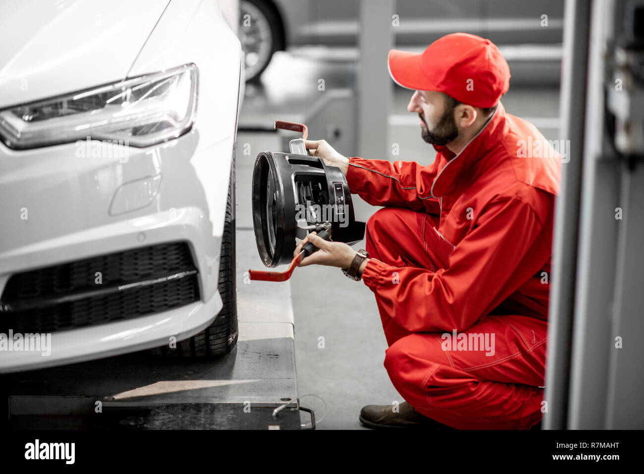 Handsome auto mechanic in red uniform fixing disk for wheel alignment at the car service Stock Photo