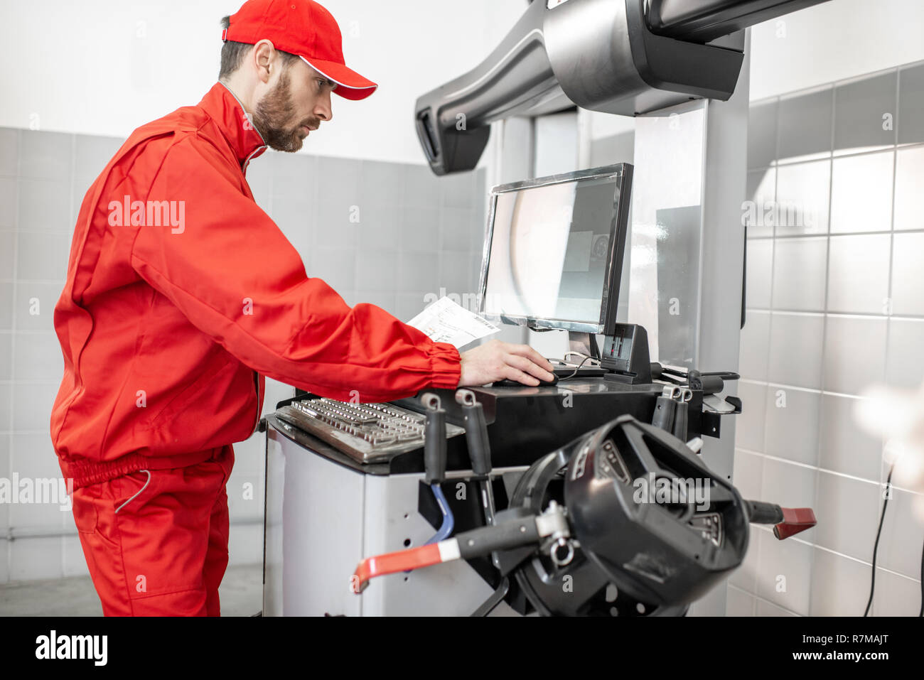 Auto mechanic in red uniform working with computer doing wheel allignment at the car service Stock Photo