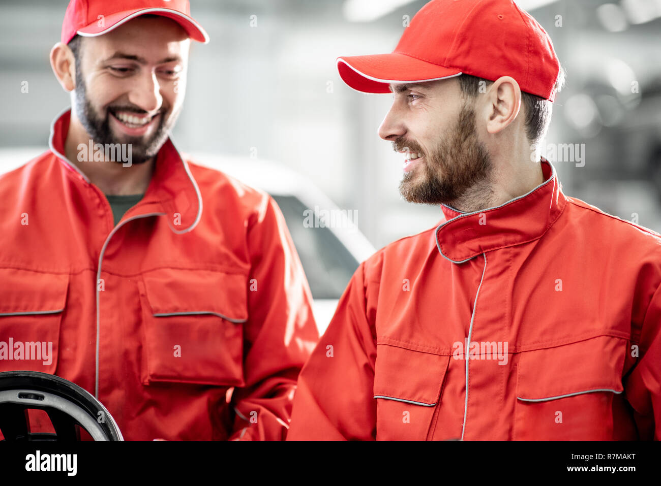 Two handsome auto mechanics in red uniform making wheel geometry with professional tools and computer at the car service Stock Photo