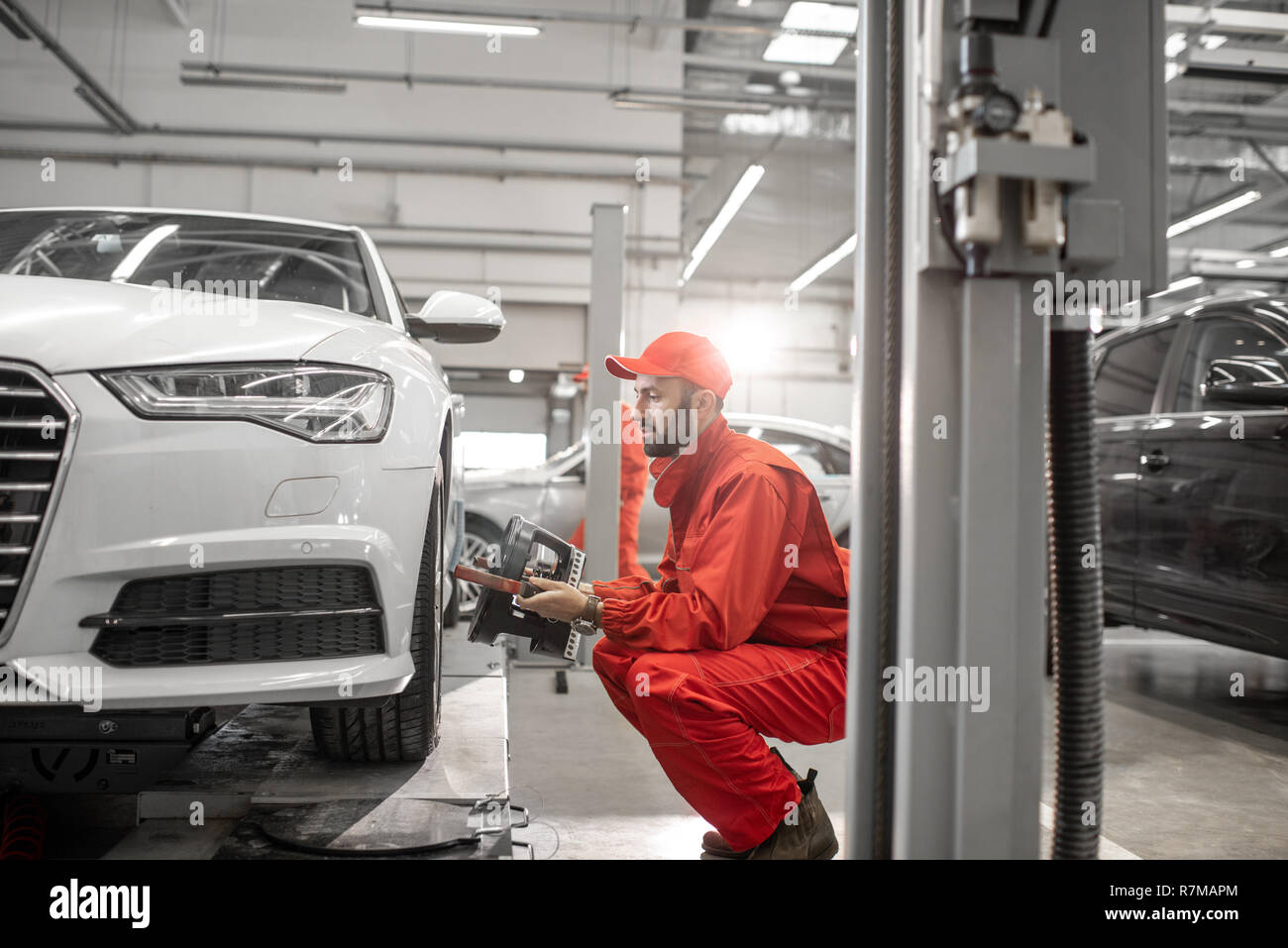 Handsome auto mechanic in red uniform fixing disk for wheel alignment at the car service Stock Photo