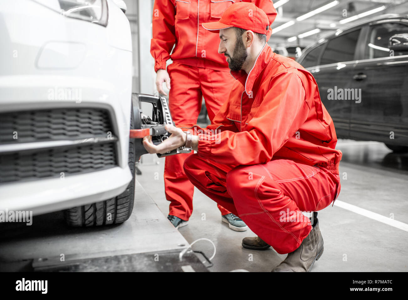 Two auto mechanics in red uniform fixing disk for wheel alignment on a