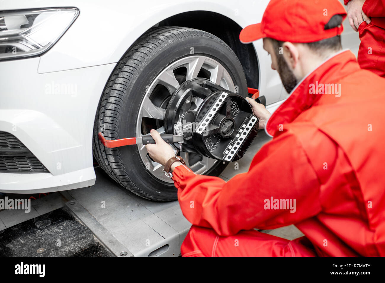 Handsome auto mechanic in red uniform fixing disk for wheel alignment at the car service Stock Photo